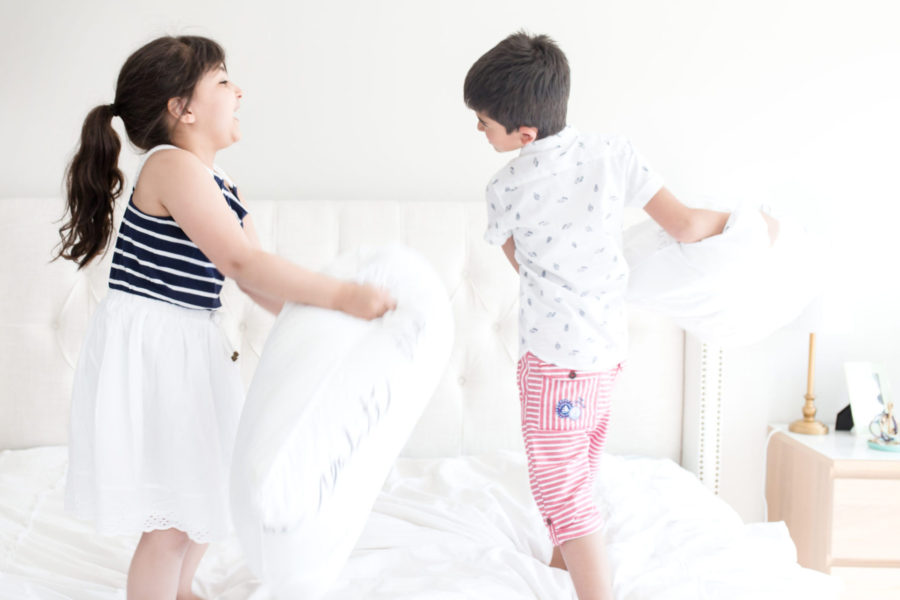 two kids having a pillow fight on a white bed. toy rotation system encouraging play.