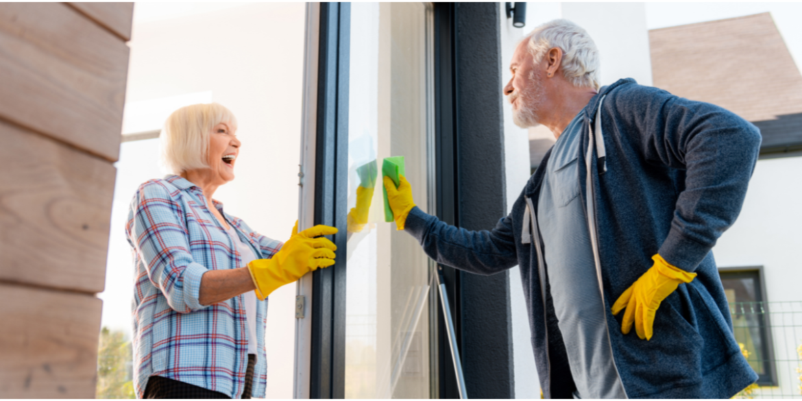  elderly lady and gentleman engaging in light housework together by washing windows 