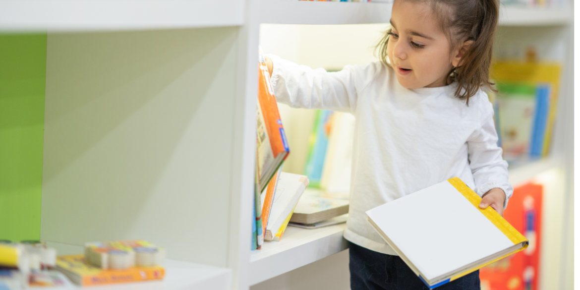 toddler girl putting away her books on the shelf