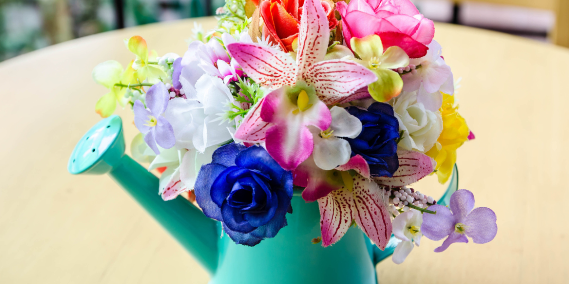 a colourful display of fake flowers in a watering can vase